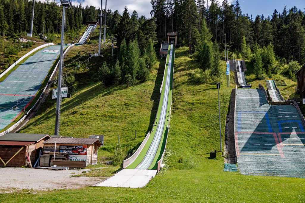 Skispringen in Ramsau am Dachstein - Ramsau am Dachstein ist Weltcup-Standort für die Skisprung-Damen und auch für die nordische Kombination der Herren. Die Schanzenanlage verfügt über Matten für den Sommer und auch ein Kuriosum, das es so wir wissen, nur einmal auf der Welt gibt: Eine Anlauf-Testspur, die hier in der Mitte zu sehen ist. - © alpintreff.de - Christian Schön